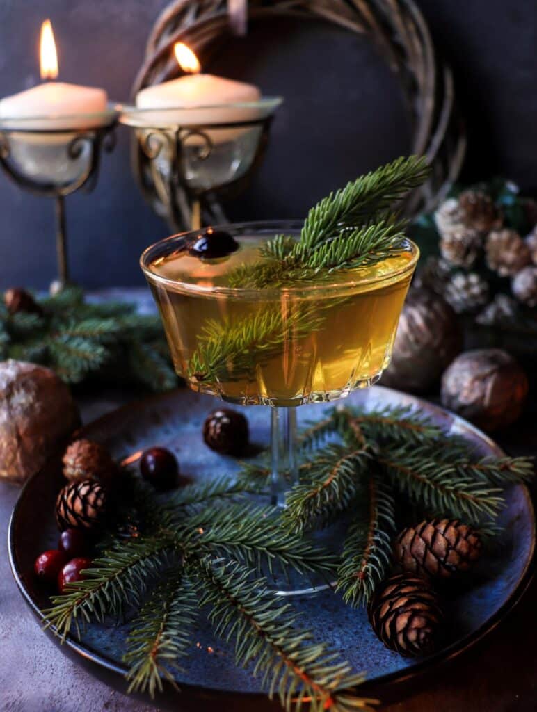 Holiday Spruce Cocktail made with spruce-infused syrup, brandy, and orange liqueur — a festive winter drink served with a spruce sprig and orange twist.