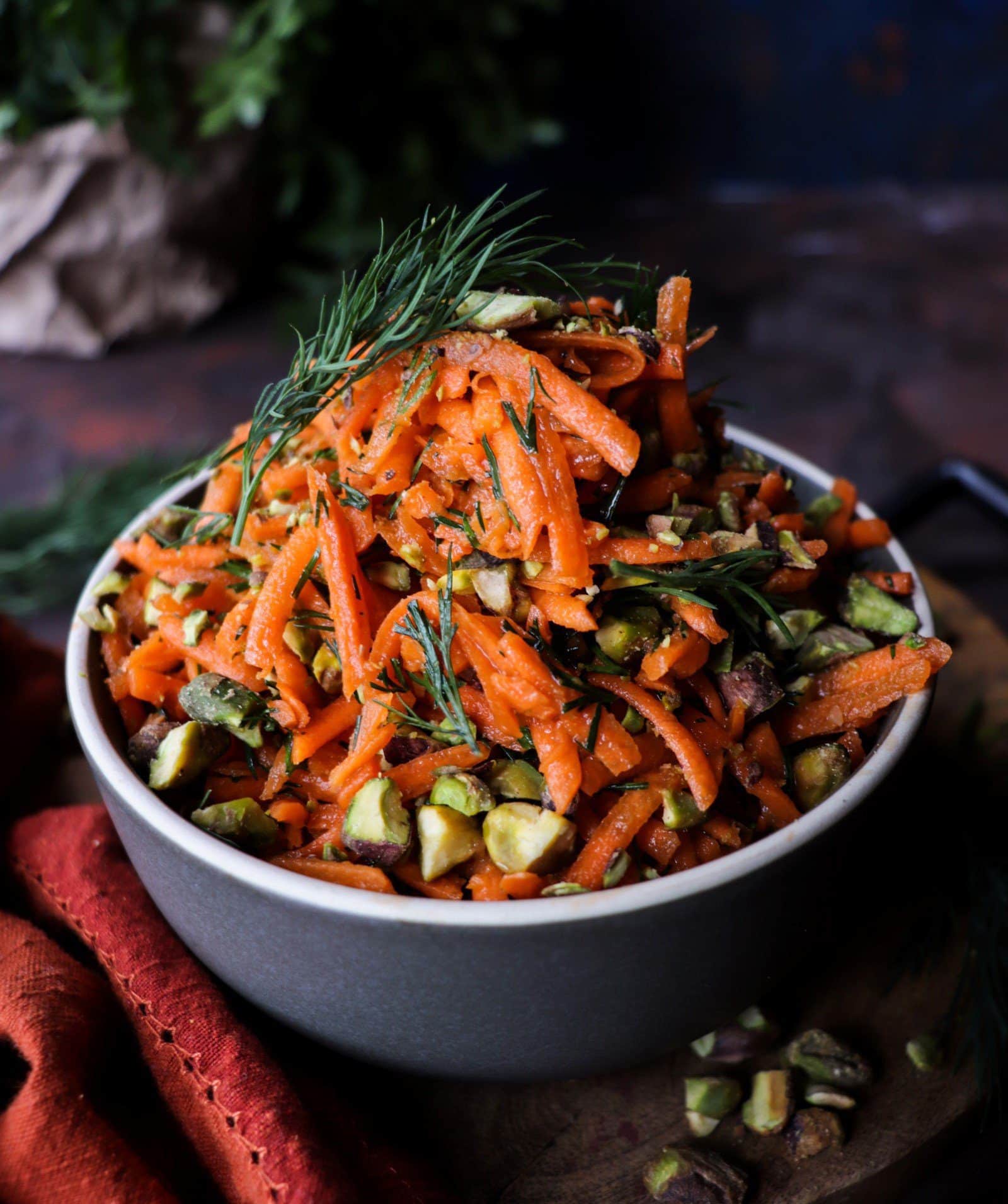 Carrot salad with pistachios and dill in a bowl, topped with chopped pistachios and fresh herbs.