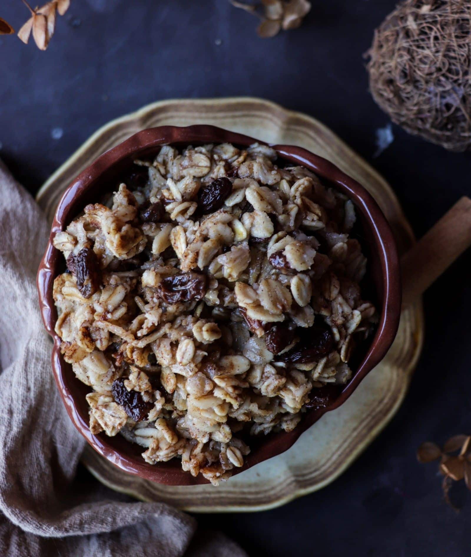 Cinnamon raisin oatmeal served in a ceramic bowl, topped with plump raisins and a cinnamon stick, styled with dried flowers, a linen cloth, and warm, cozy breakfast tones.