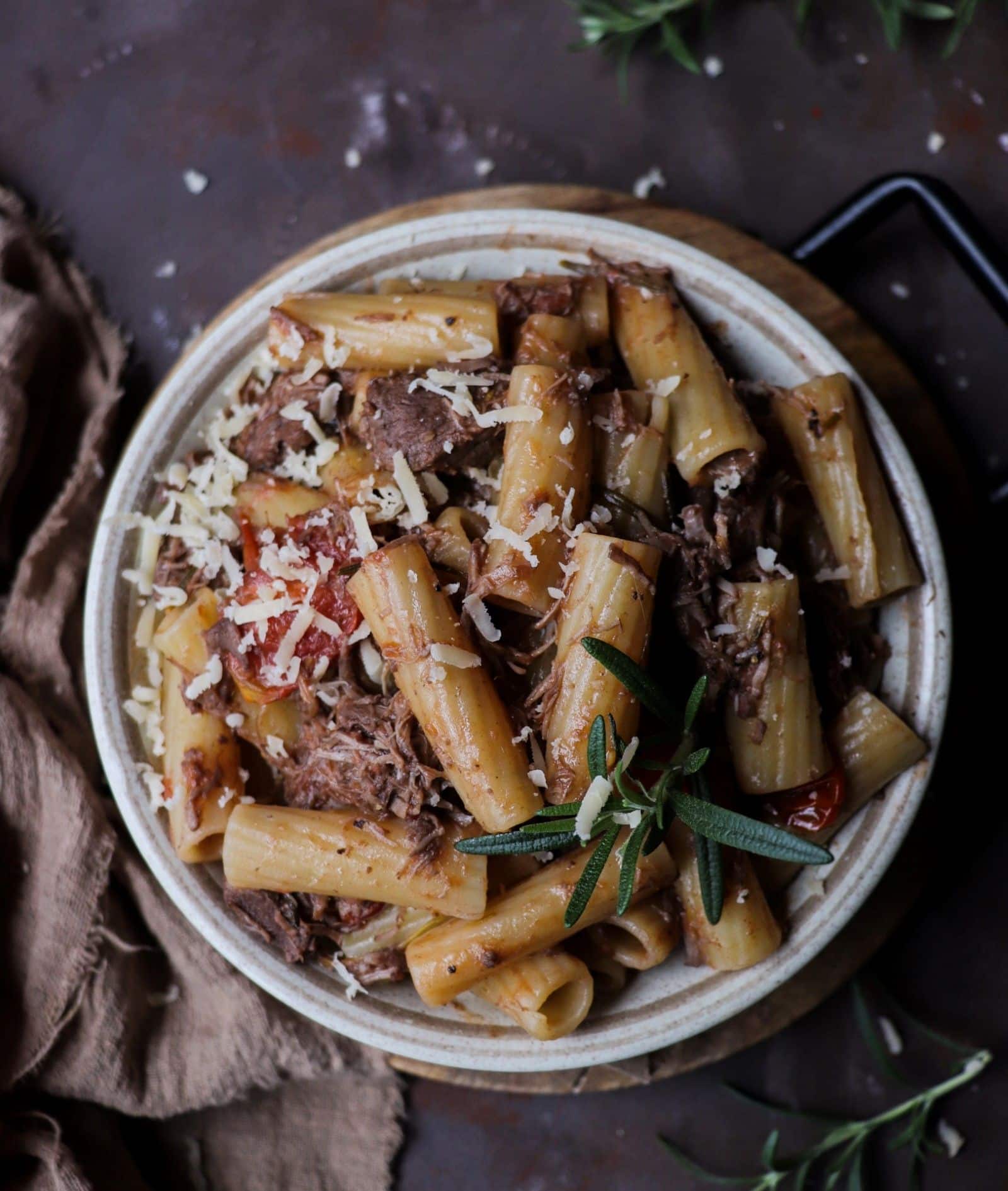 Pasta with lamb ragu served in a rustic bowl, featuring tender slow-cooked lamb, rigatoni pasta, tomatoes, rosemary, and grated cheese.
