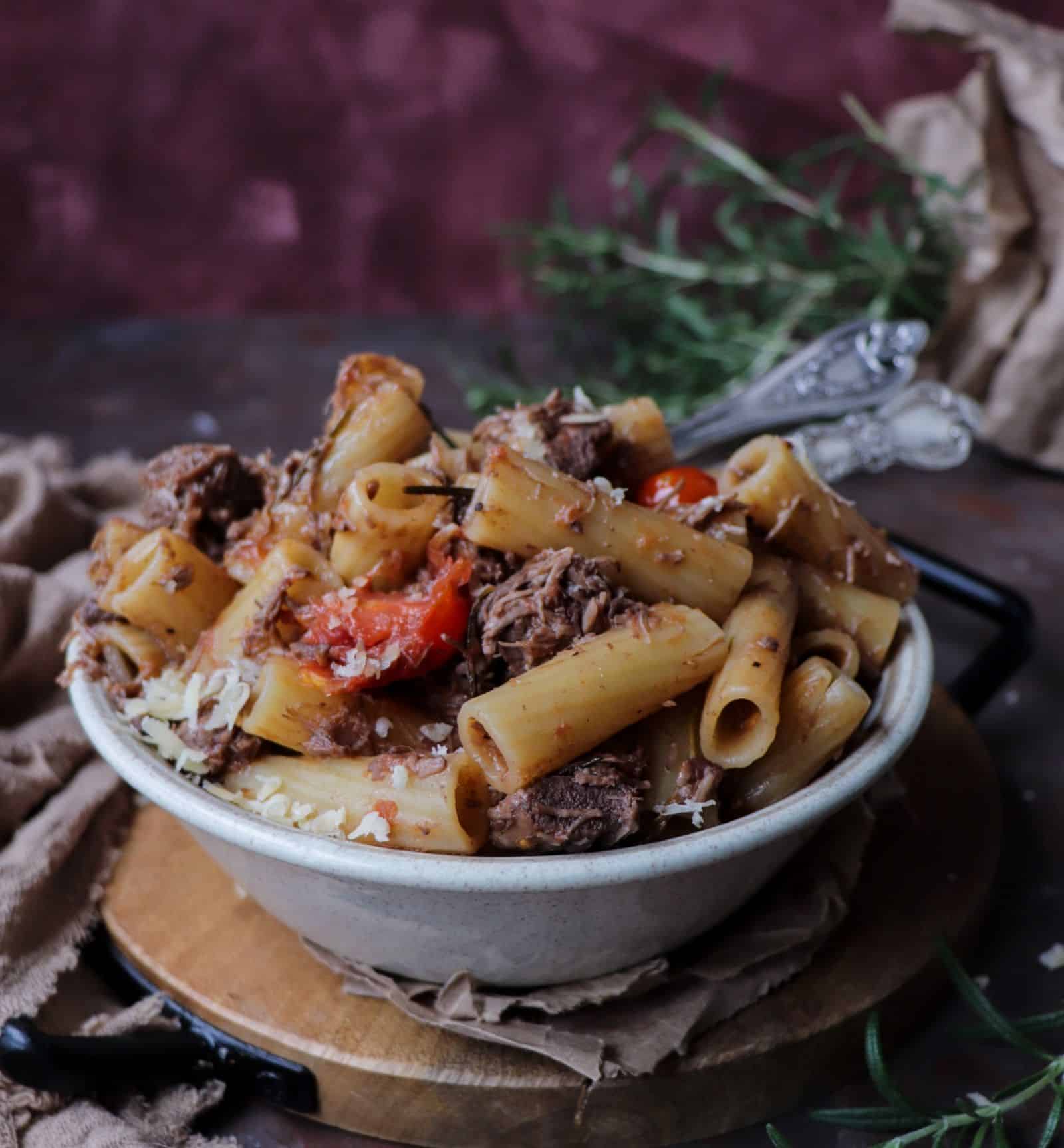 Pasta with lamb ragu served in a rustic bowl, featuring tender slow-cooked lamb, rigatoni pasta, tomatoes, rosemary, and grated cheese.