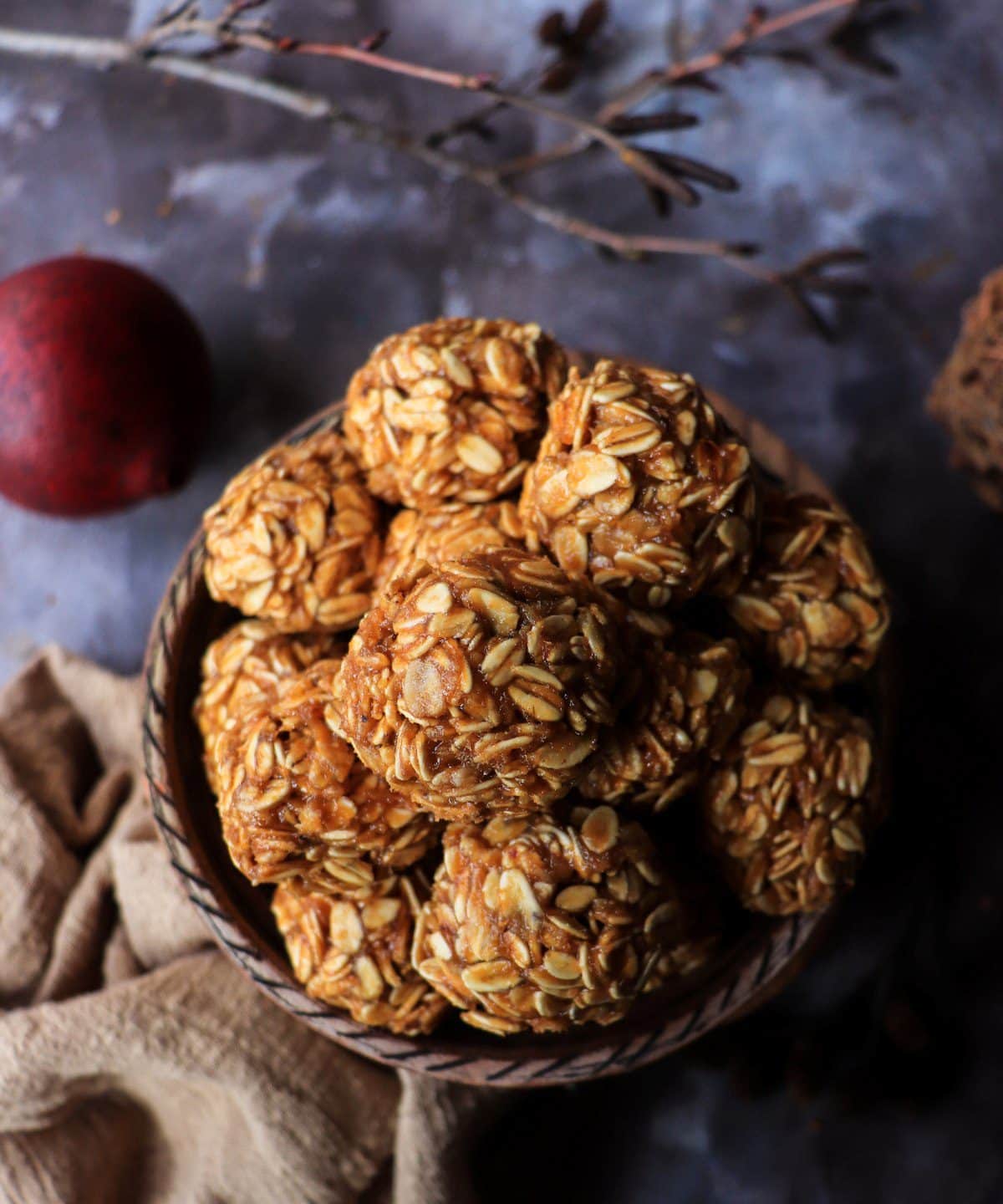 Peanut butter dulce de leche oatmeal balls stacked in a rustic ceramic bowl, showing chewy rolled oats coated in a glossy caramel-peanut mixture, styled with warm linens and moody lighting for a cozy snack presentation.