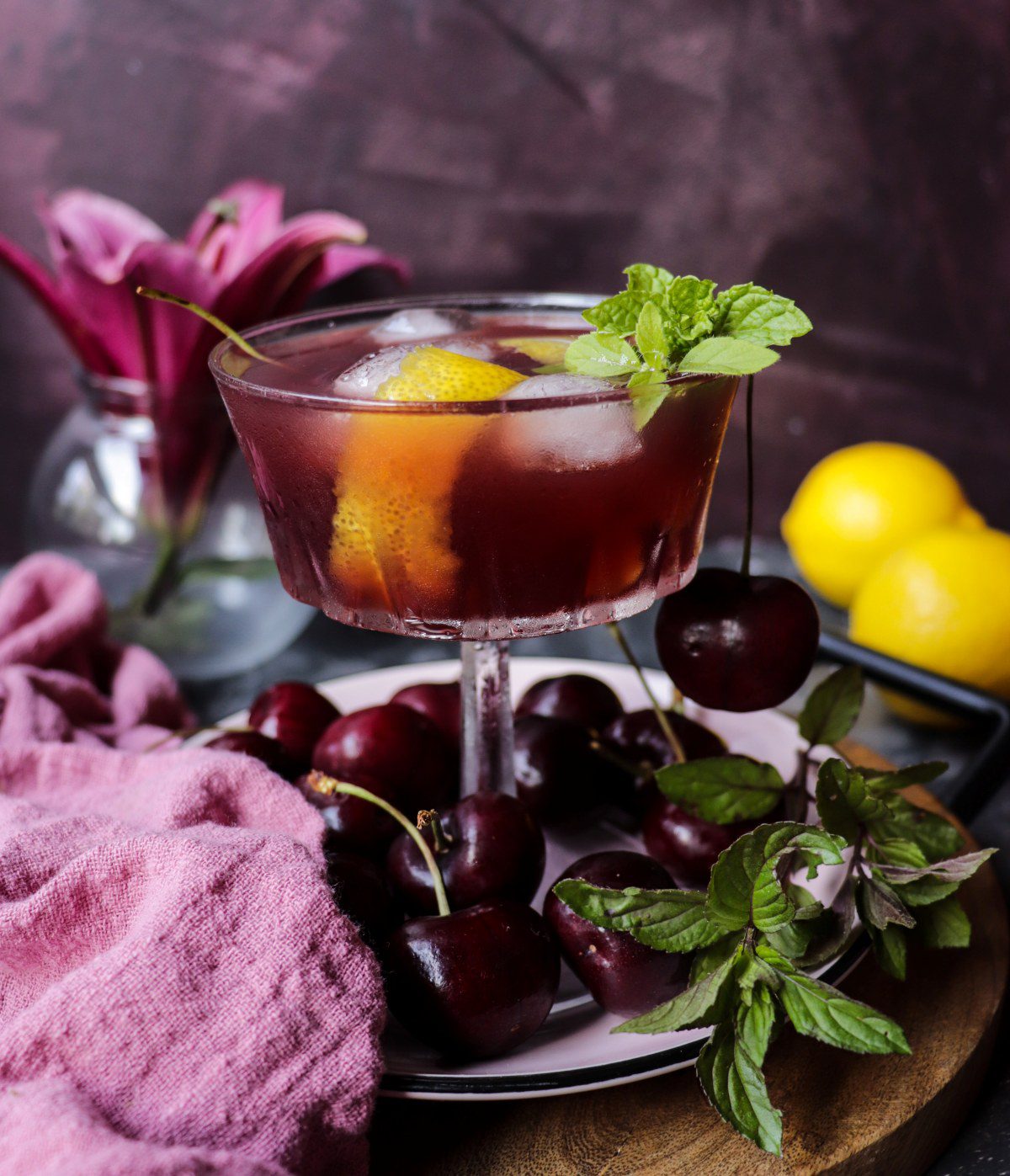 Cherry lemon amaretto cocktail with a rich red hue served over ice, garnished with lemon, mint and cherries.