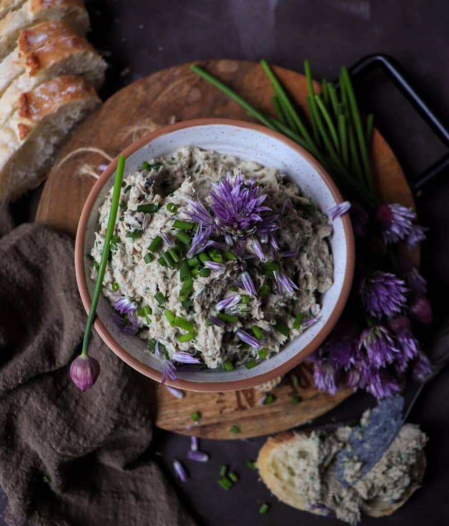 Creamy sardine spread with sour cream and chives, served in a bowl and garnished with fresh chives and chive blossoms, with bread on the side.