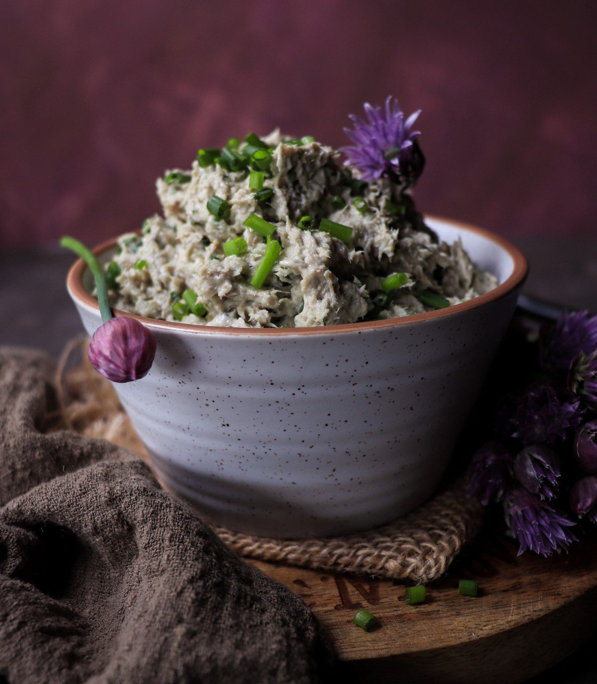 Sardine spread with sour cream and chives served in a ceramic bowl, garnished with chive blossoms and chopped chives, with sliced bread on the side.