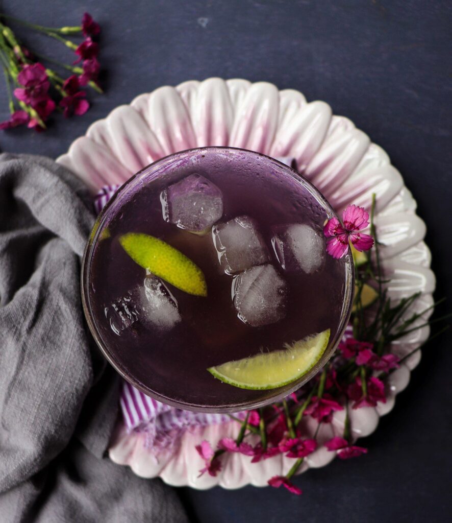 Top view of a violet cocktail with ice and citrus slices showing a deep purple colour in an elegant coupe glass.