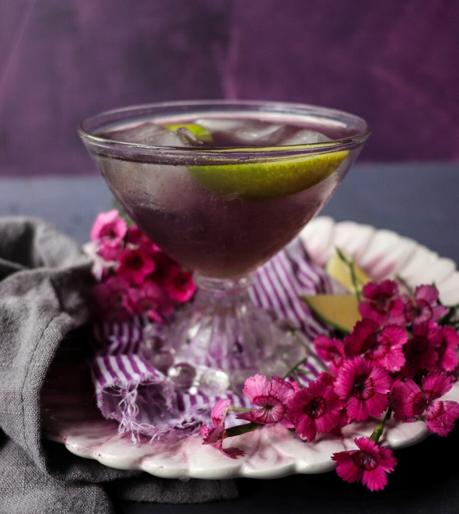 Violet cocktail with Crème de Violette and lime served in a coupe glass with a rich purple hue and floral garnish.