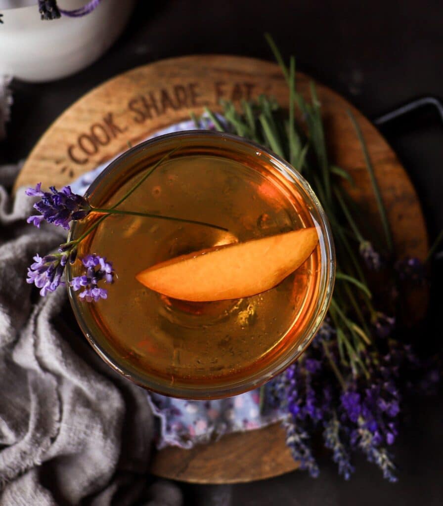 Apricot lavender cocktail with gin and apricot brandy in a coupe glass, garnished with fresh lavender, styled with dried lavender bundles and a soft pink linen backdrop.