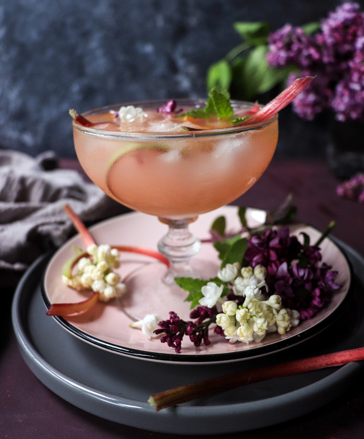 Rhubarb cocktail with honey, citrus slice, and flowers served in a coupe glass over ice