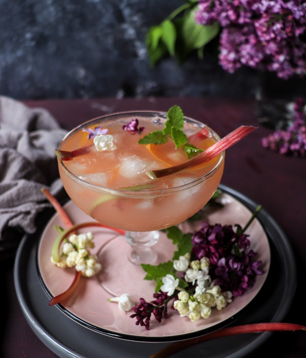Rhubarb honey cocktail in a coupe glass with ice, citrus slice, and floral garnish