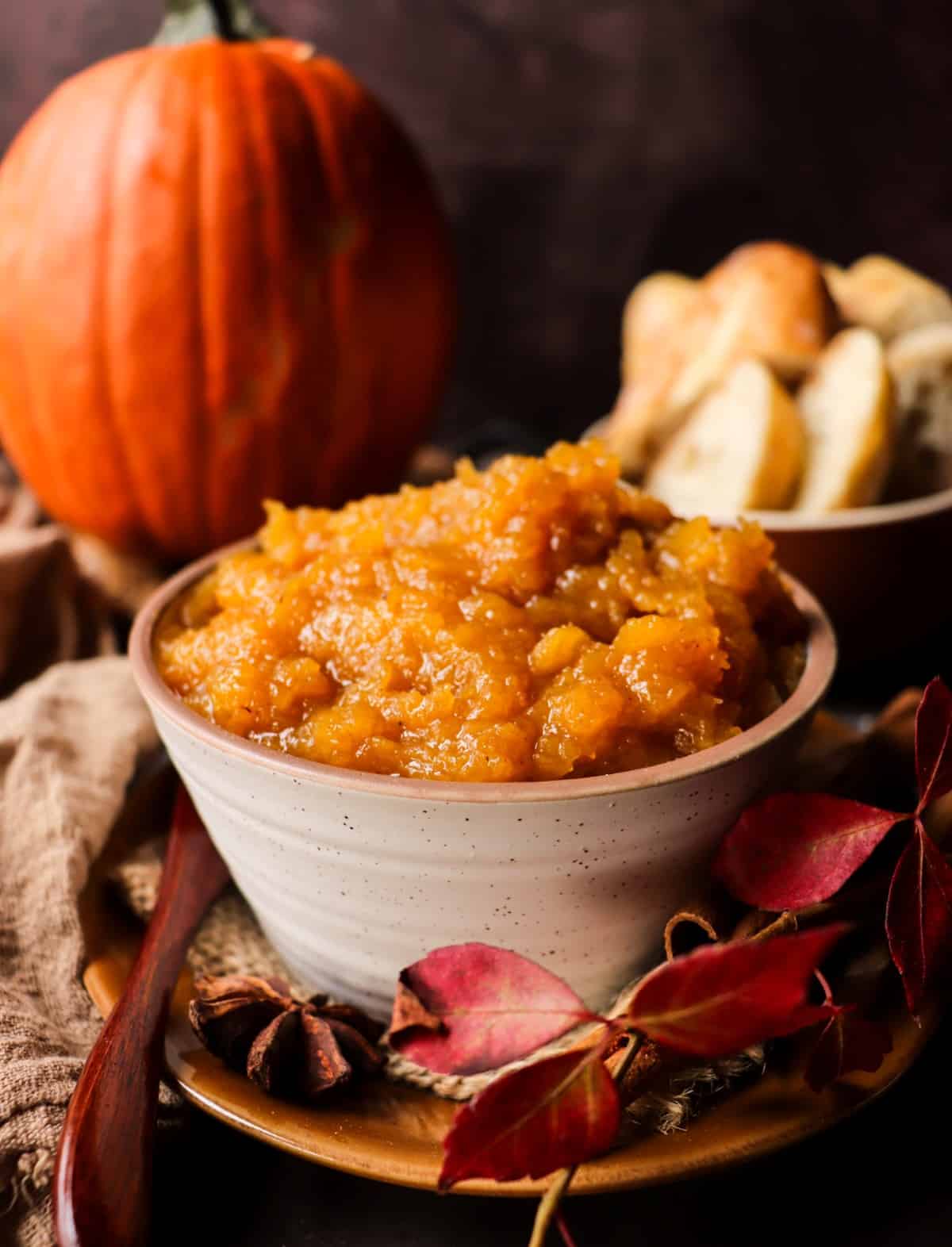 A jar of Low Sugar Spiced Pumpkin Jam recipe with Brandy surrounded by cinnamon sticks and star anise, showing its golden-orange hue and chunky, glossy texture.