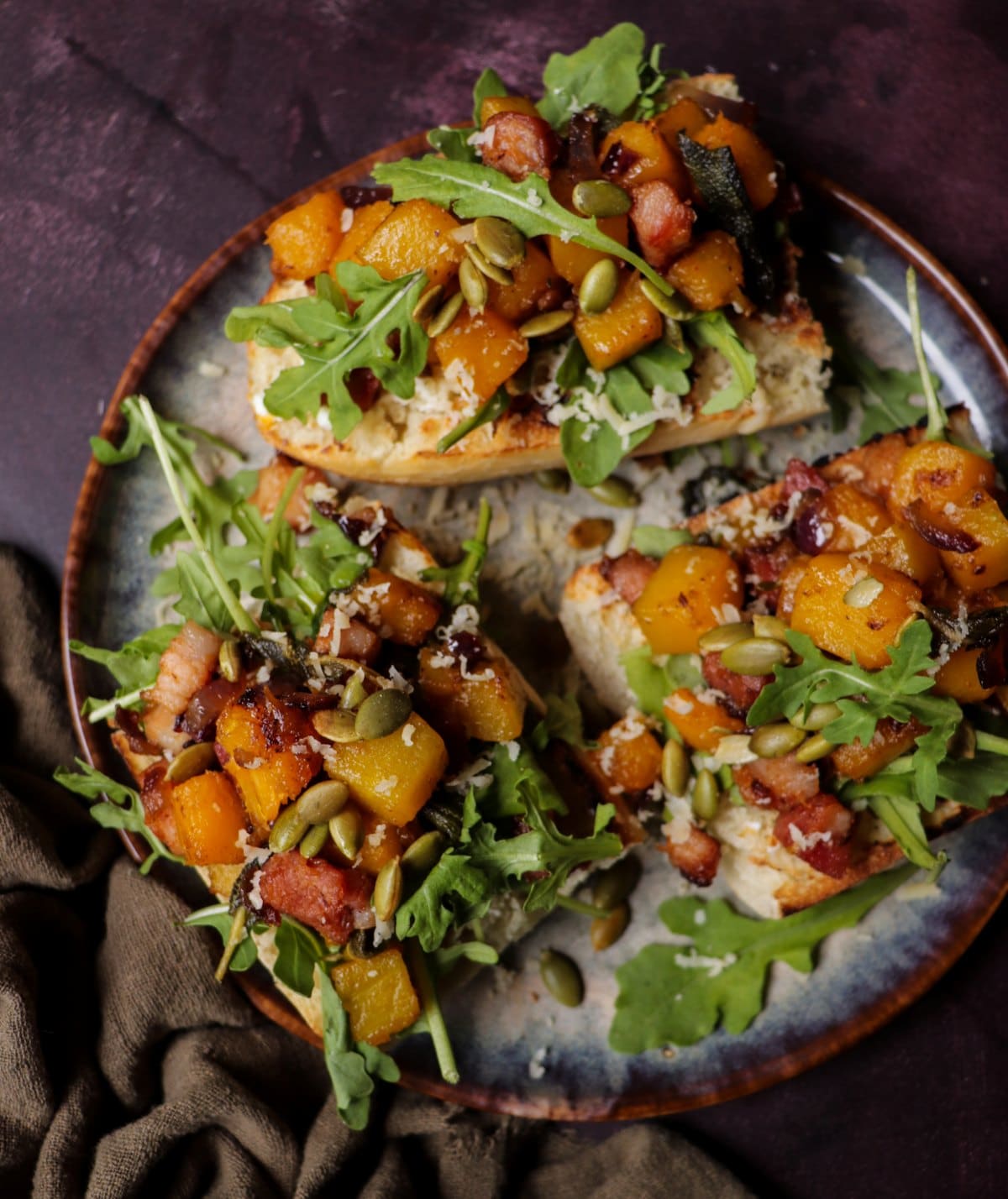 Roasted Butternut Squash Bruschetta topped with crispy ham, sage, goat cheese, and arugula on toasted bread slices — a warm and cozy fall appetizer.