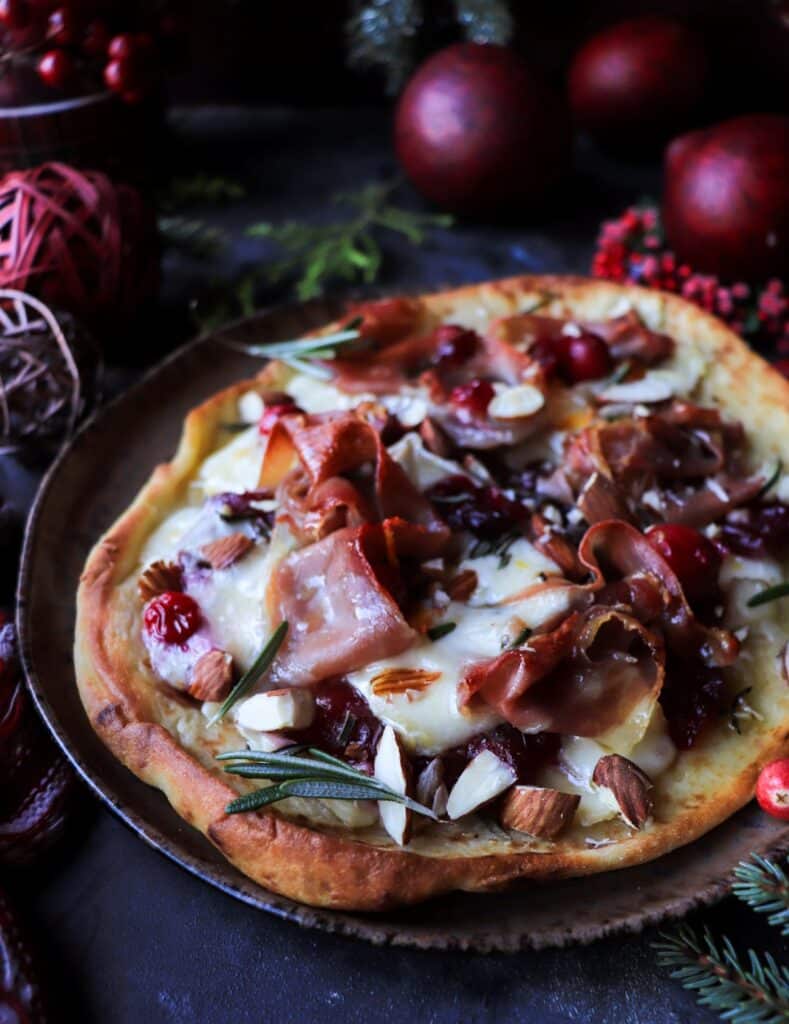 Festive naan flatbread topped with cranberry sauce, creamy brie, and crispy prosciutto, perfect for a quick holiday appetizer.