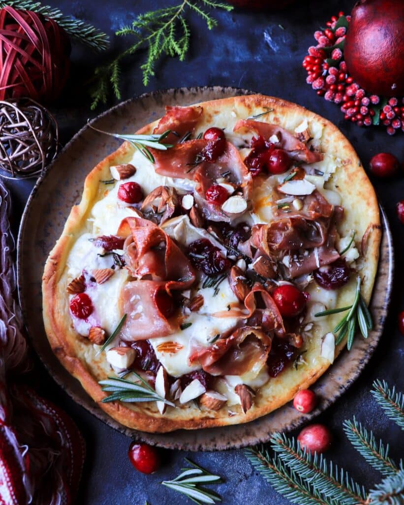 Overhead view of cranberry brie prosciutto flatbread with almonds, rosemary, and bright cranberries, sliced and ready to serve for holiday entertaining.