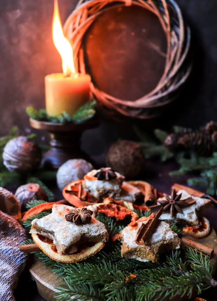 Rustic scene of almond gingerbread star cookies on a dark background with pine branches and a glowing candle in the distance.
