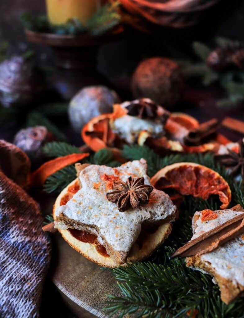 Festive Orange Almond Gingerbread Cookies arranged on a rustic wooden board with dried oranges, cinnamon sticks, and evergreen sprigs under warm candlelight
