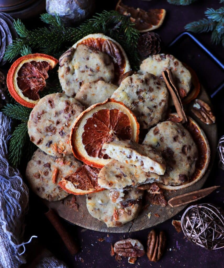 Cozy holiday scene with orange pecan toffee shortbread cookies on a rustic board, decorated with dried oranges, pecans, and Christmas greenery.