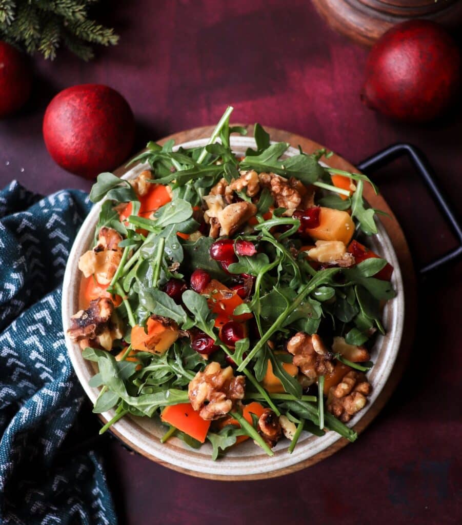 Top view of a Persimmon Pomegranate Walnut Salad with arugula, pomegranate arils, and toasted walnuts — a fresh and colourful festive salad.