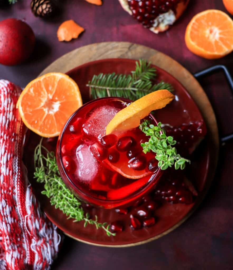 Overhead view of pomegranate clementine holiday sangria filled with pomegranate seeds, citrus slices, and ice, garnished with fresh thyme.
