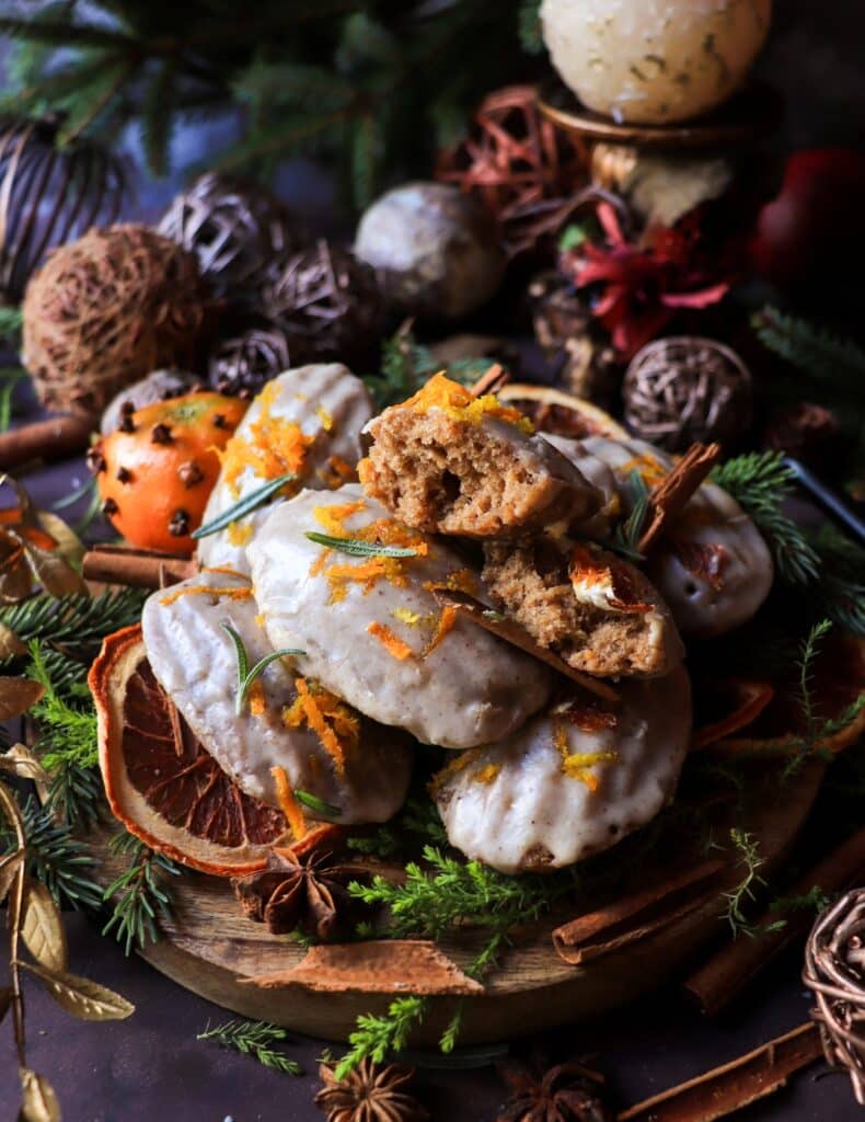 Spiced orange madeleines with brandy glaze, including one madeleine cut open to show the tender spiced crumb, styled with dried citrus, rosemary, and festive holiday decor.