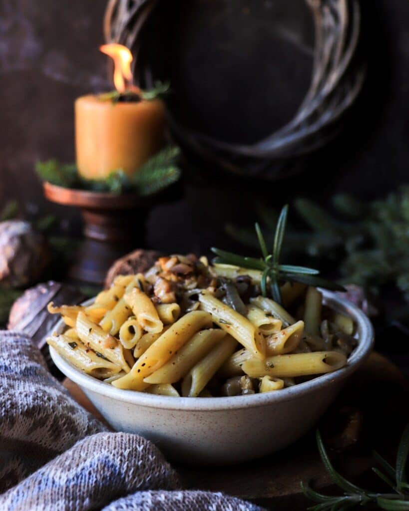 Close-up of caramelized onion and chestnut pasta, showing golden onions, chestnuts, and fresh rosemary coating the pasta.