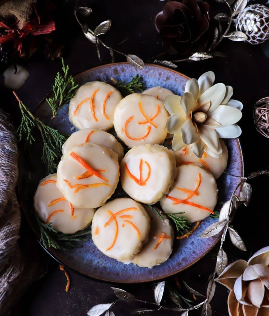Clementine shortbread cookies with brandy glaze arranged on a blue plate with fresh clementine zest.