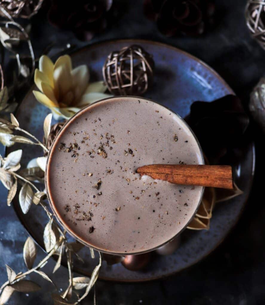 Top-down shot of an eggnog brandy alexander cocktail with a smooth, creamy surface and a dusting of nutmeg, styled with golden foliage, ornaments, and soft floral accents for a festive holiday setting.