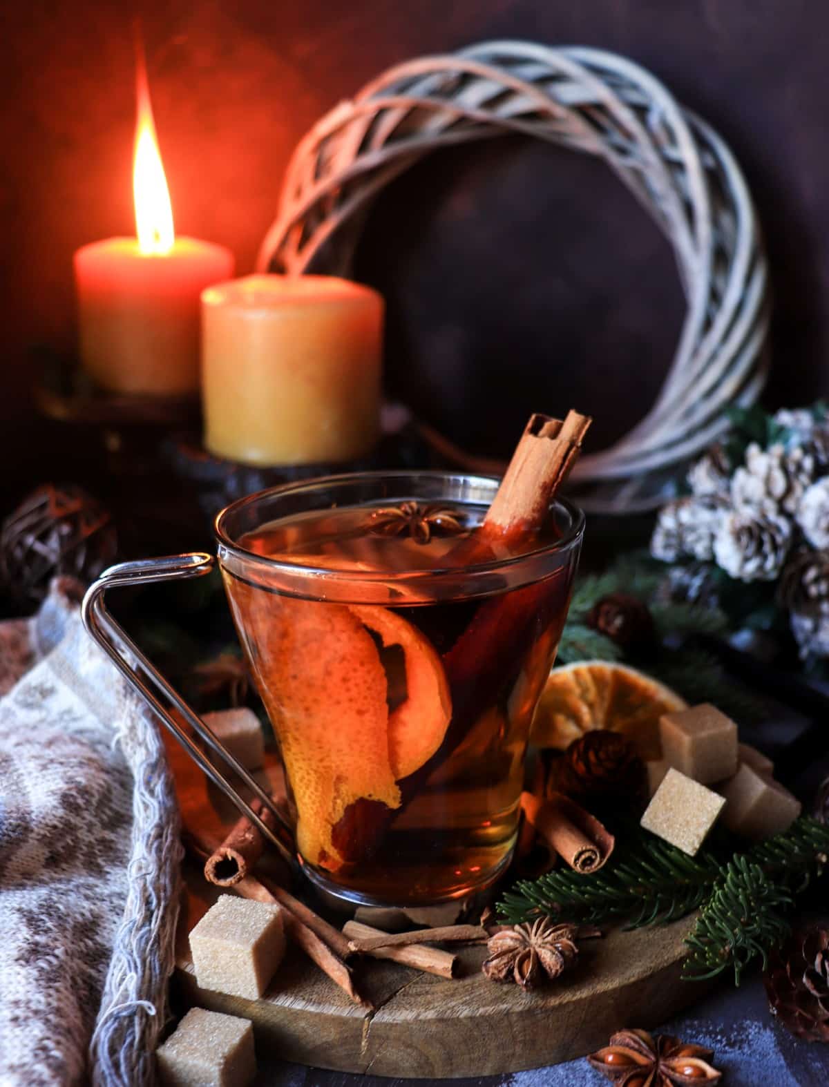 Festive clementine mulled rum in a glass mug, styled with cinnamon, citrus peel, glowing candles, and evergreen branches for a cosy Christmas atmosphere.