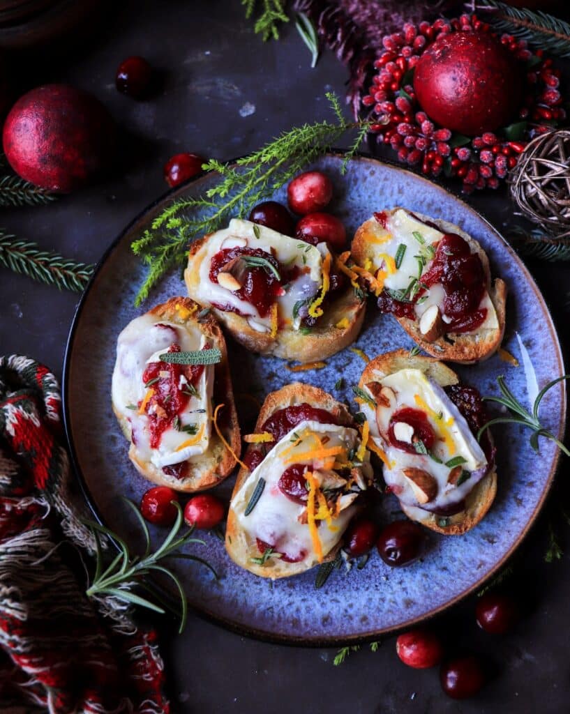 Festive cranberry brie crostini served warm on toasted baguette, styled with glowing candlelight, fresh rosemary, and evergreen accents for a cosy Christmas atmosphere.