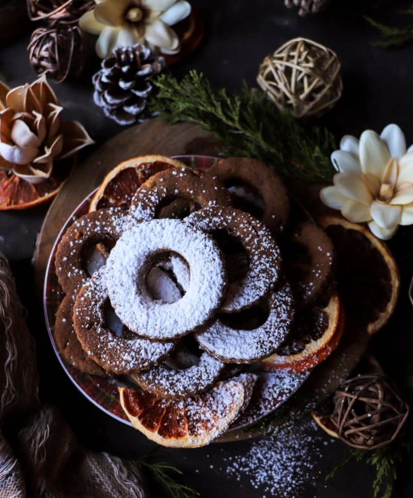 Overhead view of gluten-free rye shortbread cookies topped with powdered sugar, styled on a holiday plate with dried citrus and seasonal décor.