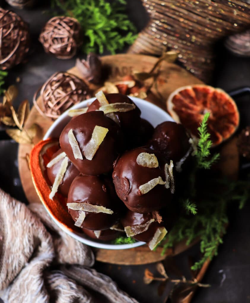 Overhead view of soft chocolate gingerbread cookies with orange and rum, coated in glossy chocolate glaze and garnished with crystallized ginger on a festive dark background.