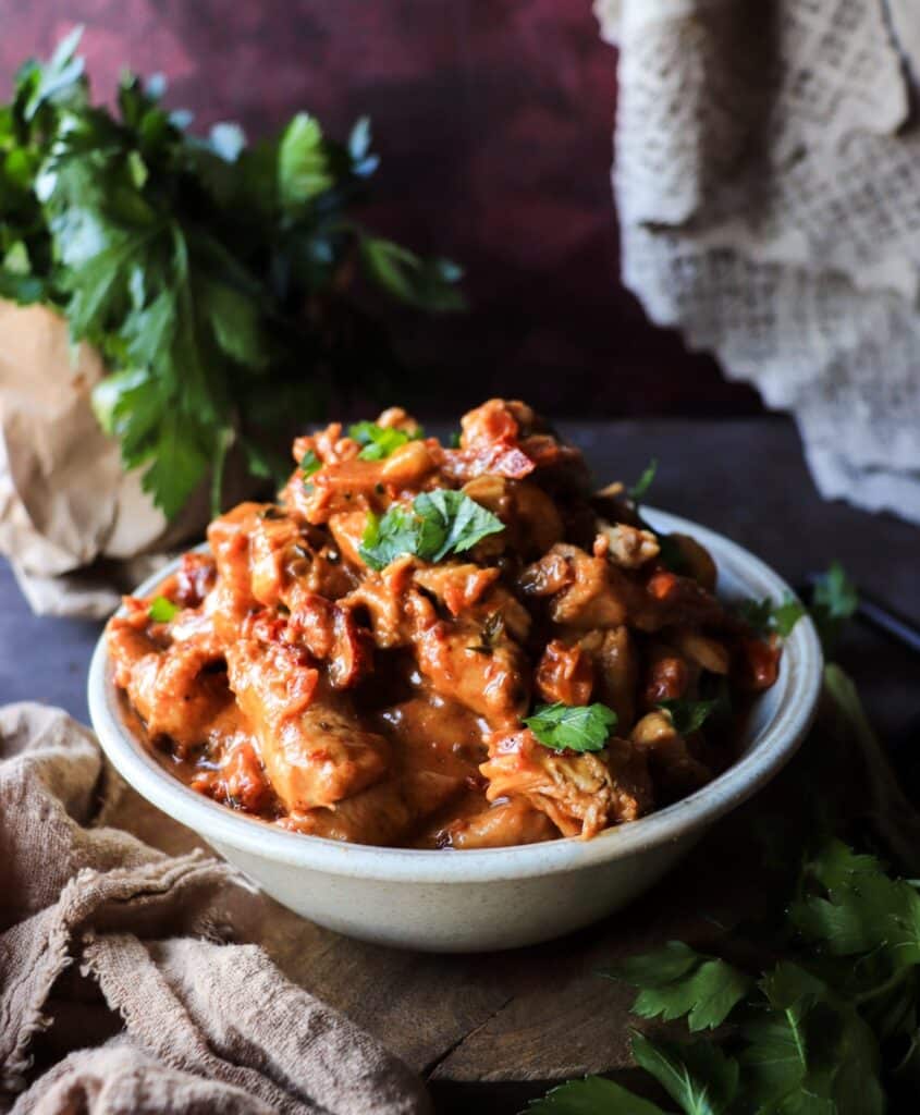 Creamy Marry Me Chicken skillet with sliced chicken breasts, sun-dried tomatoes, and herbs, photographed from an angled view on a rustic surface.