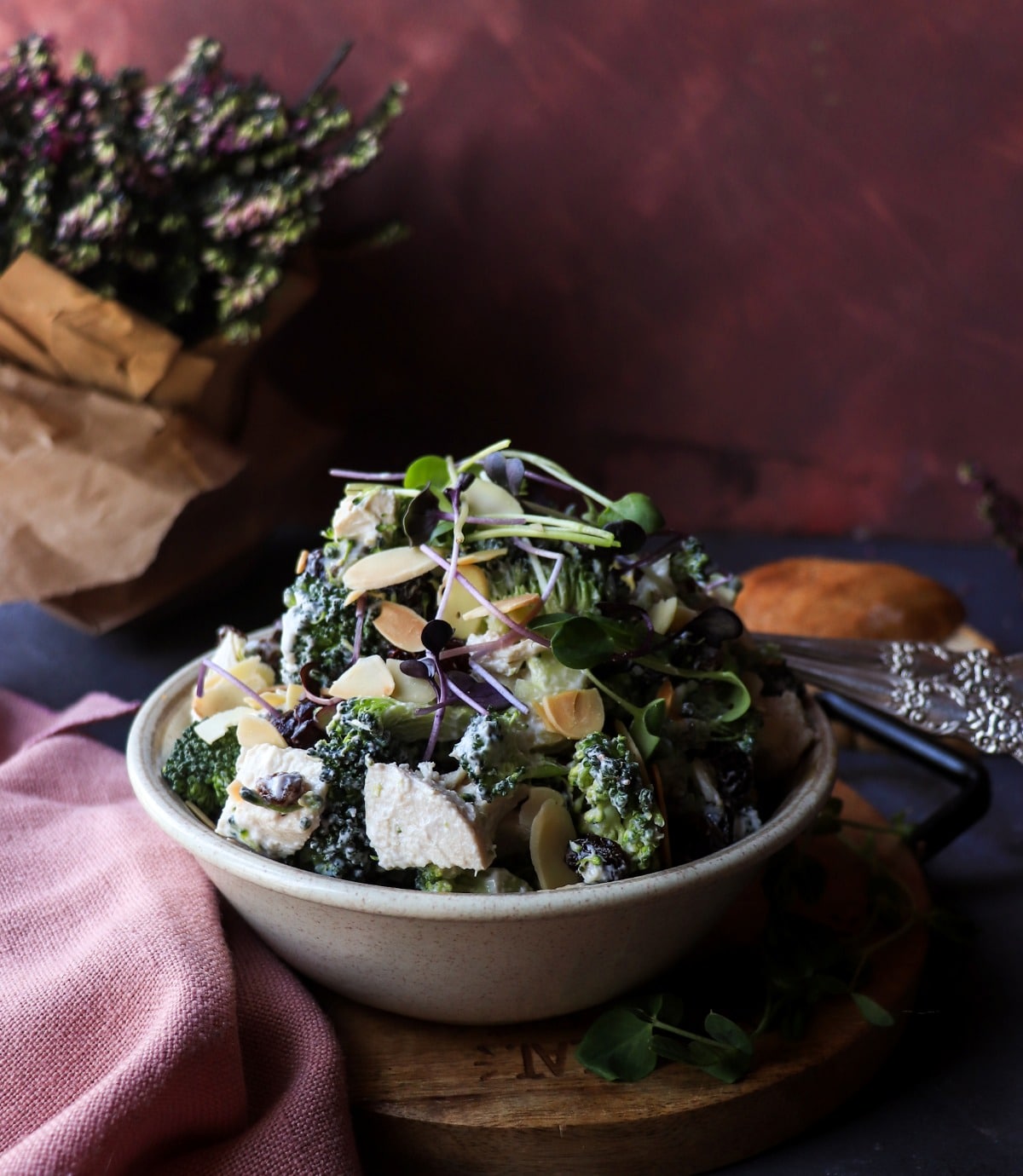 Raw Broccoli Salad with Chicken, Almonds, and Dried Fruit served in a bowl, topped with microgreens and a light yogurt dressing.