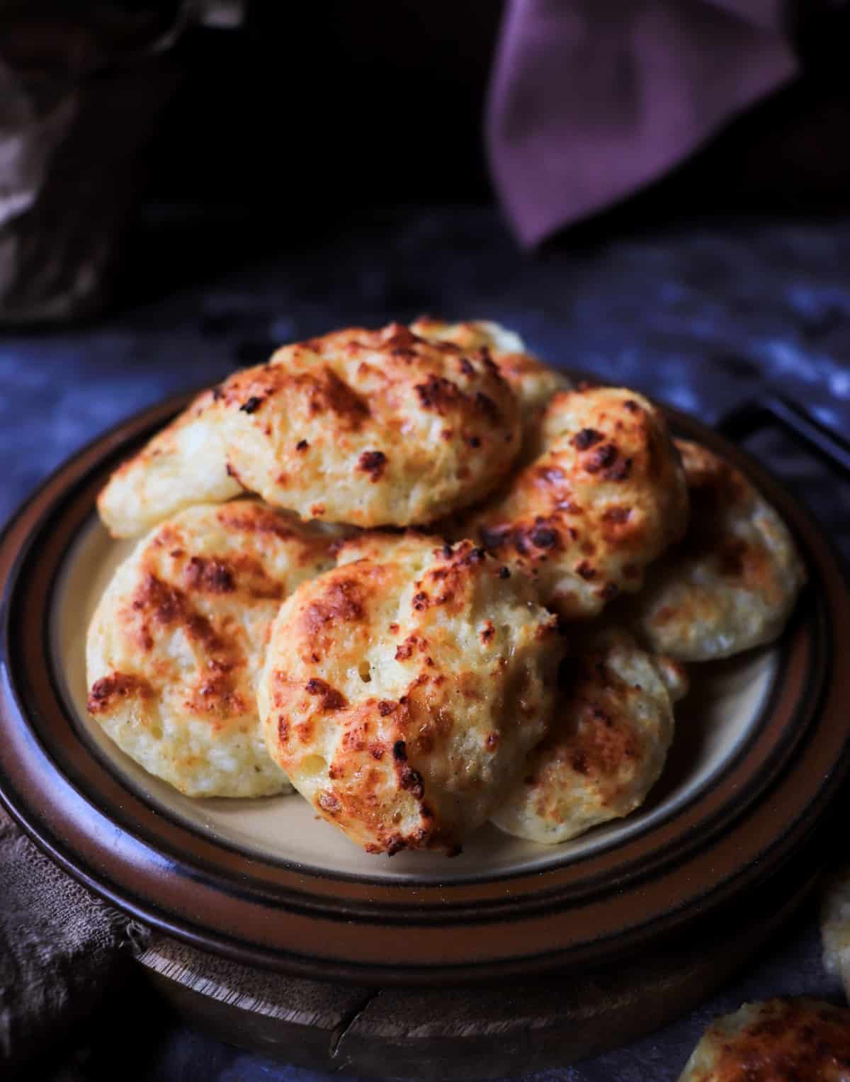 Golden baked cottage cheese biscuits stacked on a rustic plate, showing a lightly browned crust and airy texture.