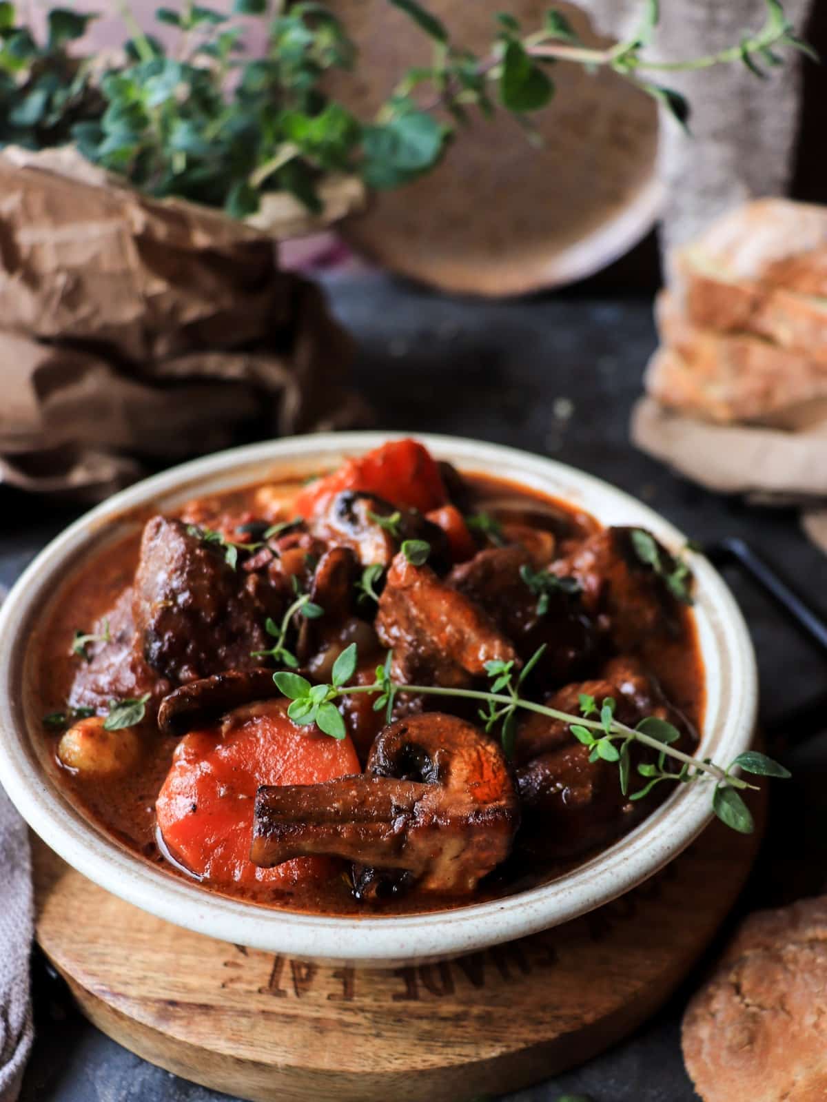 Beef Bourguignon in a rustic bowl with tender braised beef, carrots, mushrooms, and rich red wine sauce, garnished with fresh thyme and served with bread.