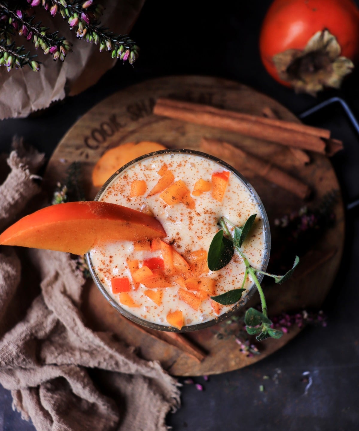 Creamy persimmon smoothie with Greek yogurt and cinnamon in a glass, topped with diced persimmon and a slice, with whole Fuyu persimmons in the background.