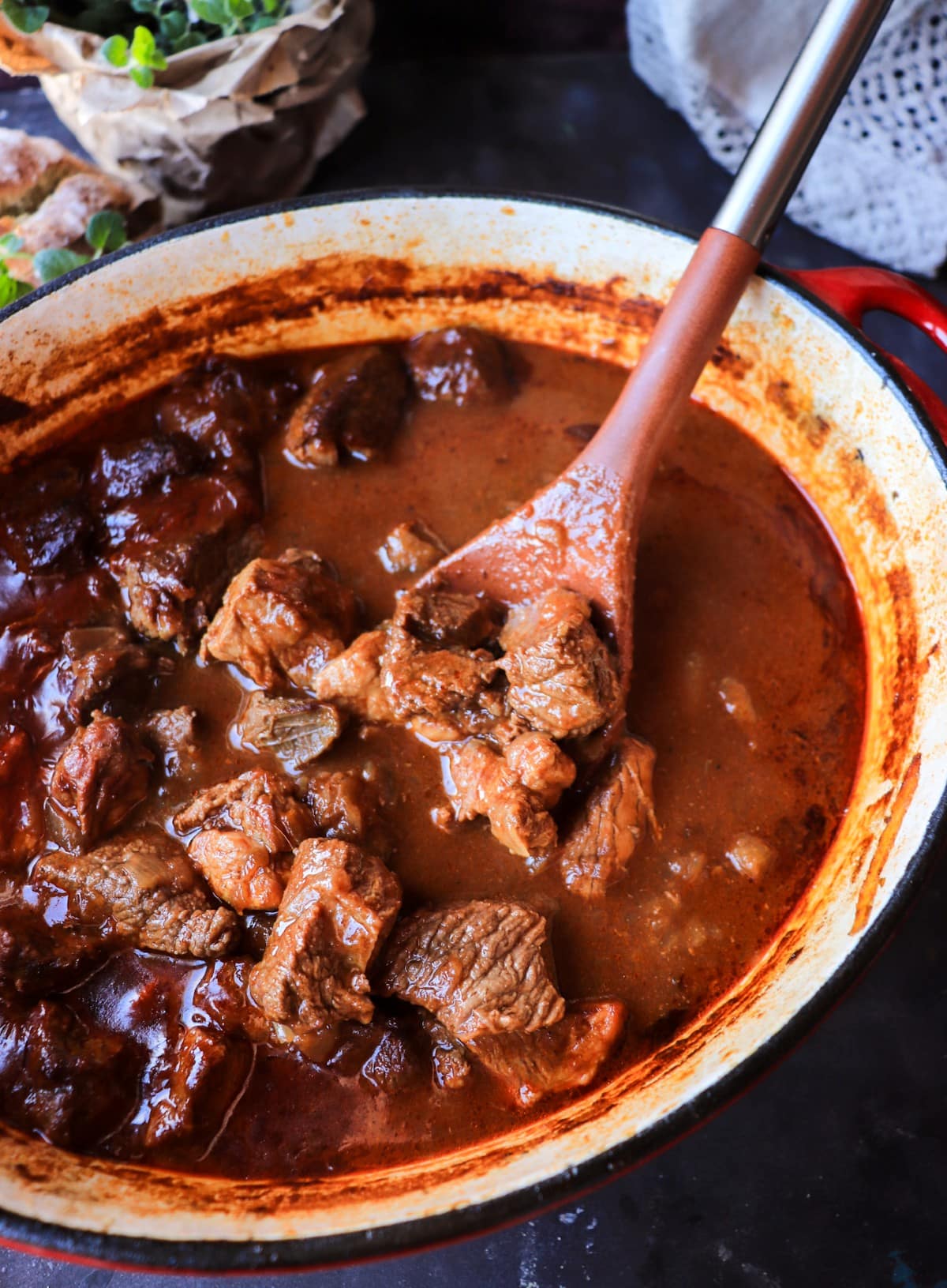 Croatian meat stew simmering in a Dutch oven with ladle, showing its brothy paprika base.