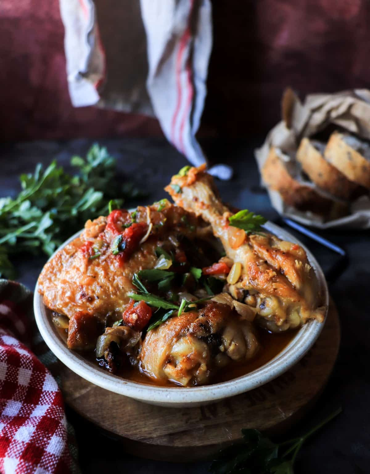 Traditional Chicken Cacciatore (Pollo alla Cacciatora) in a rustic ceramic bowl with tomato sauce and fresh parsley, styled on a wooden board with red cloth.