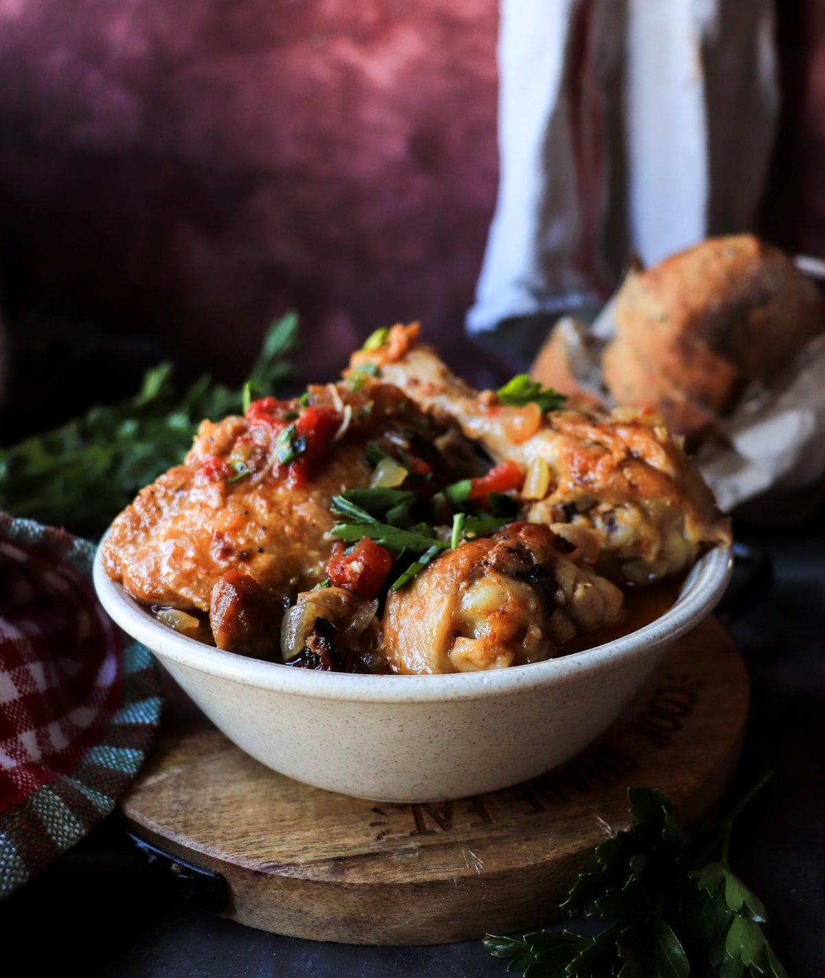 Traditional Chicken Cacciatore (Pollo alla Cacciatora) in a rustic ceramic bowl with tomato sauce and fresh parsley, styled on a wooden board with red cloth.
