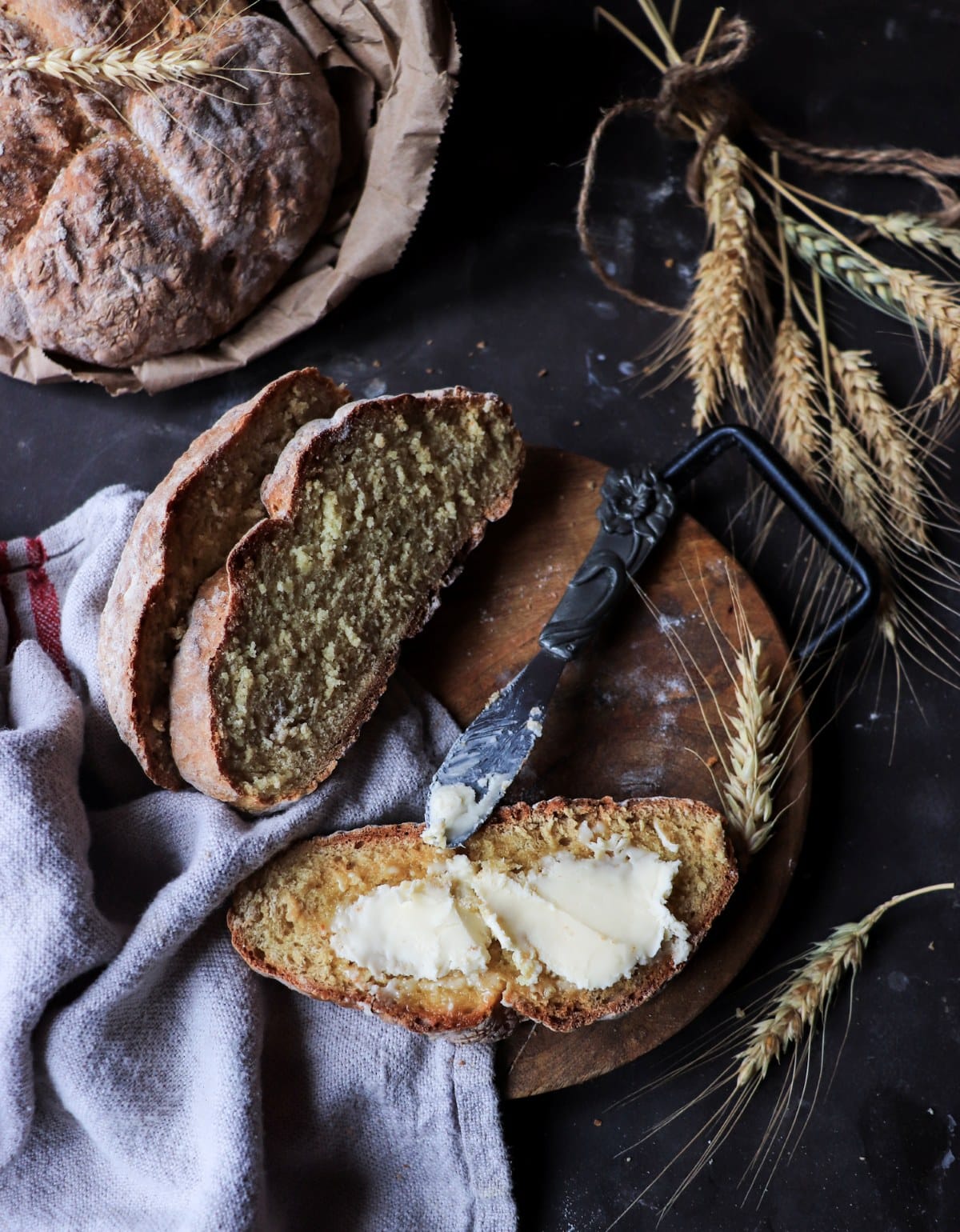 Sliced Irish soda bread with butter on a wooden board, showing a tender crumb and rustic flour-dusted crust.