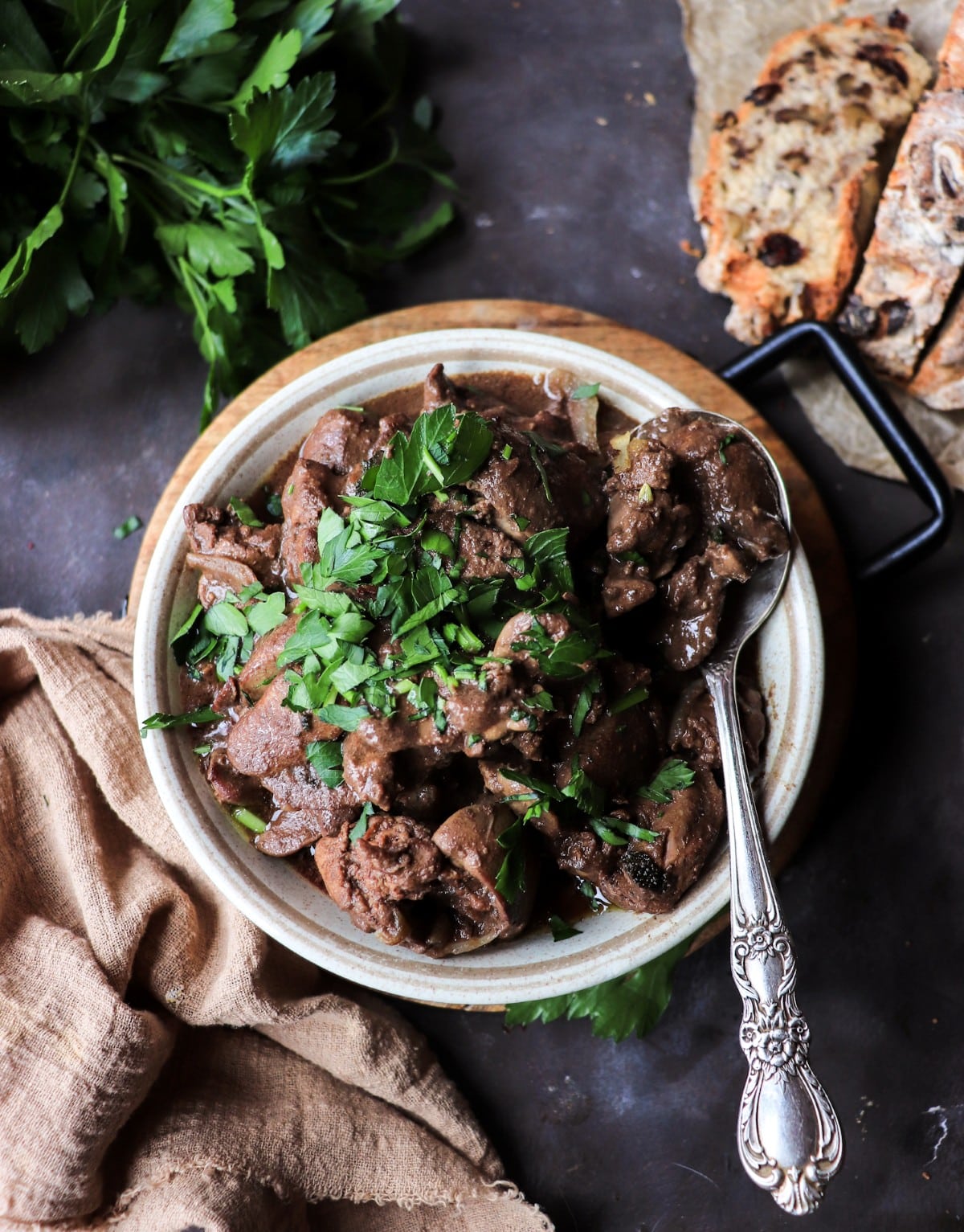 Chicken Liver Marsala in a rustic bowl topped with fresh parsley, served with crusty bread in the background.