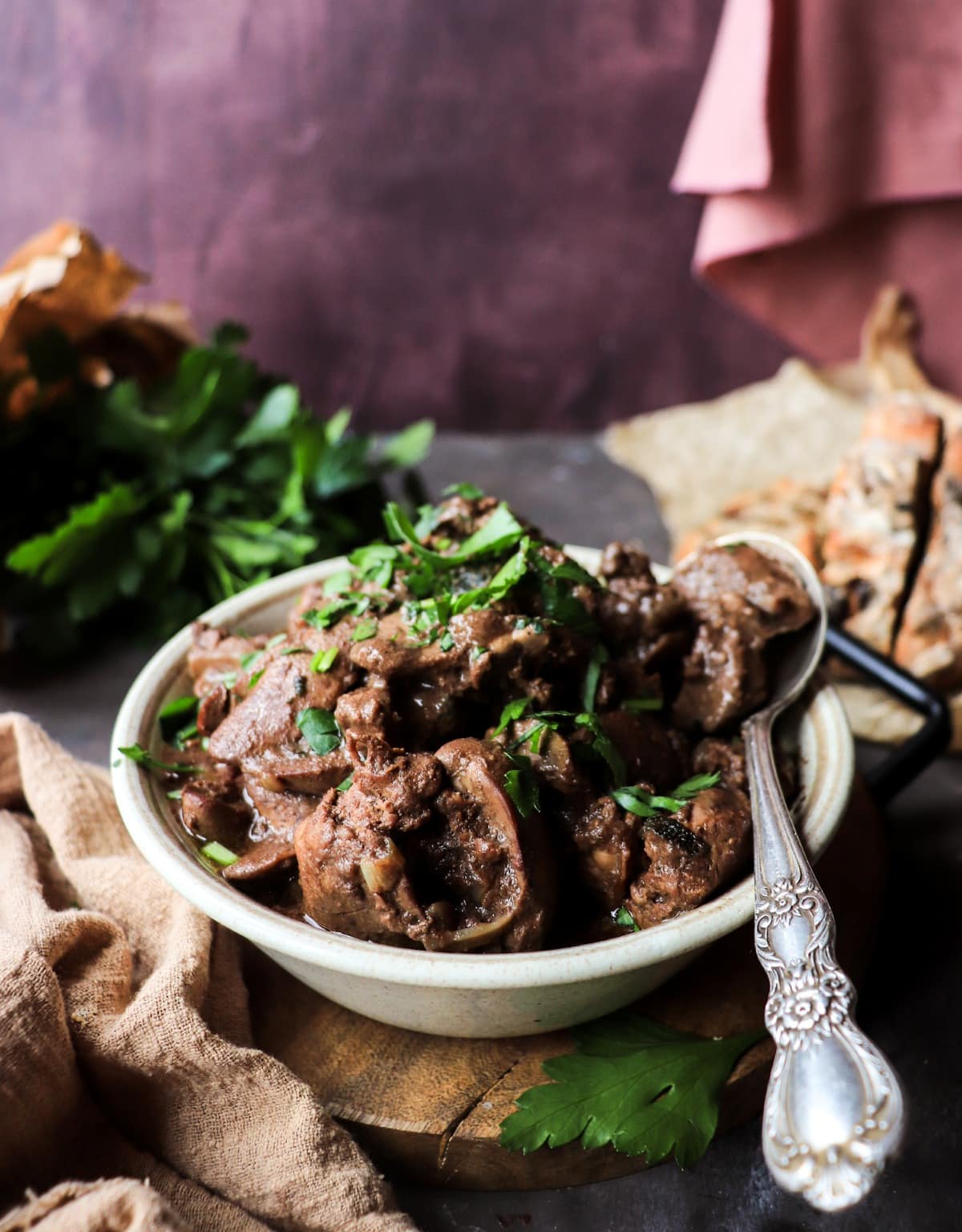 Chicken Liver Marsala in a rustic bowl topped with fresh parsley, served with crusty bread in the background.