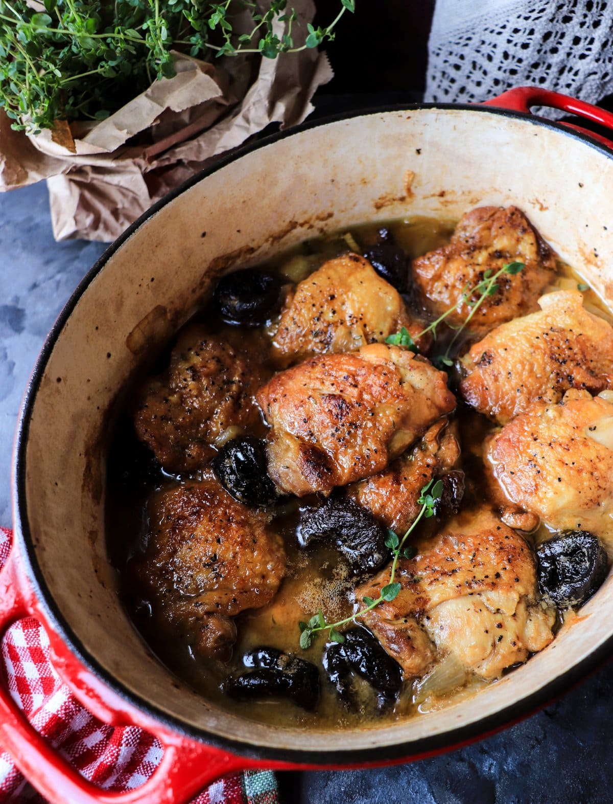 Poulet aux Pruneaux braising in a Dutch oven with bone-in chicken thighs, prunes, onions, and thyme.
