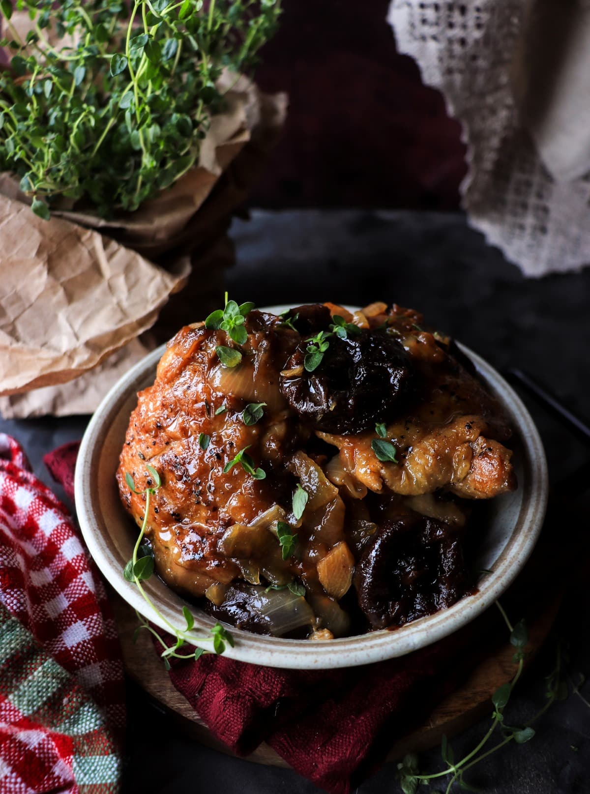 French braised chicken with prunes served in a rustic bowl with thyme garnish and wine reduction sauce.