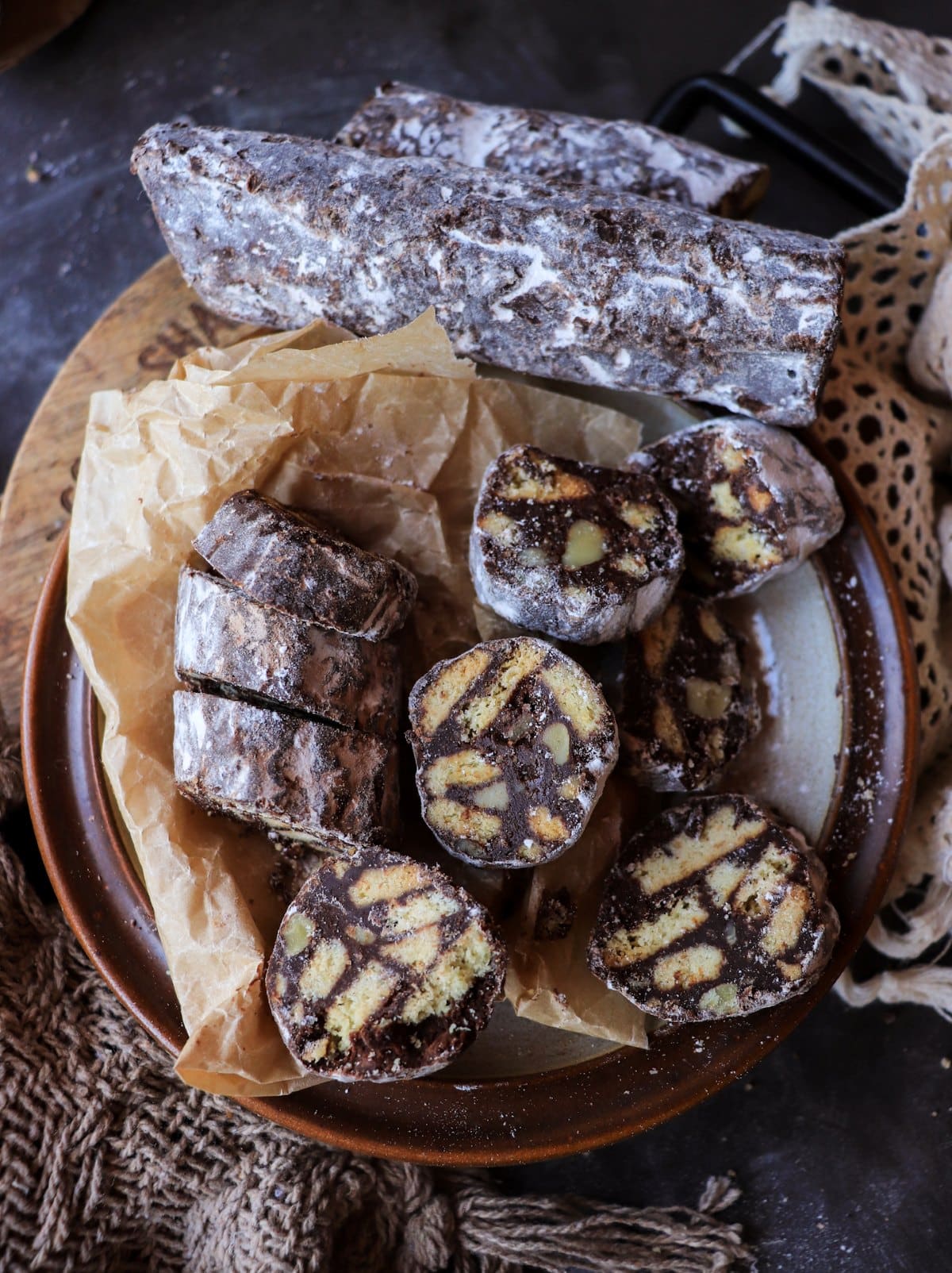 Rustic Italian chocolate salami served on a brown plate with powdered sugar coating and mosaic interior