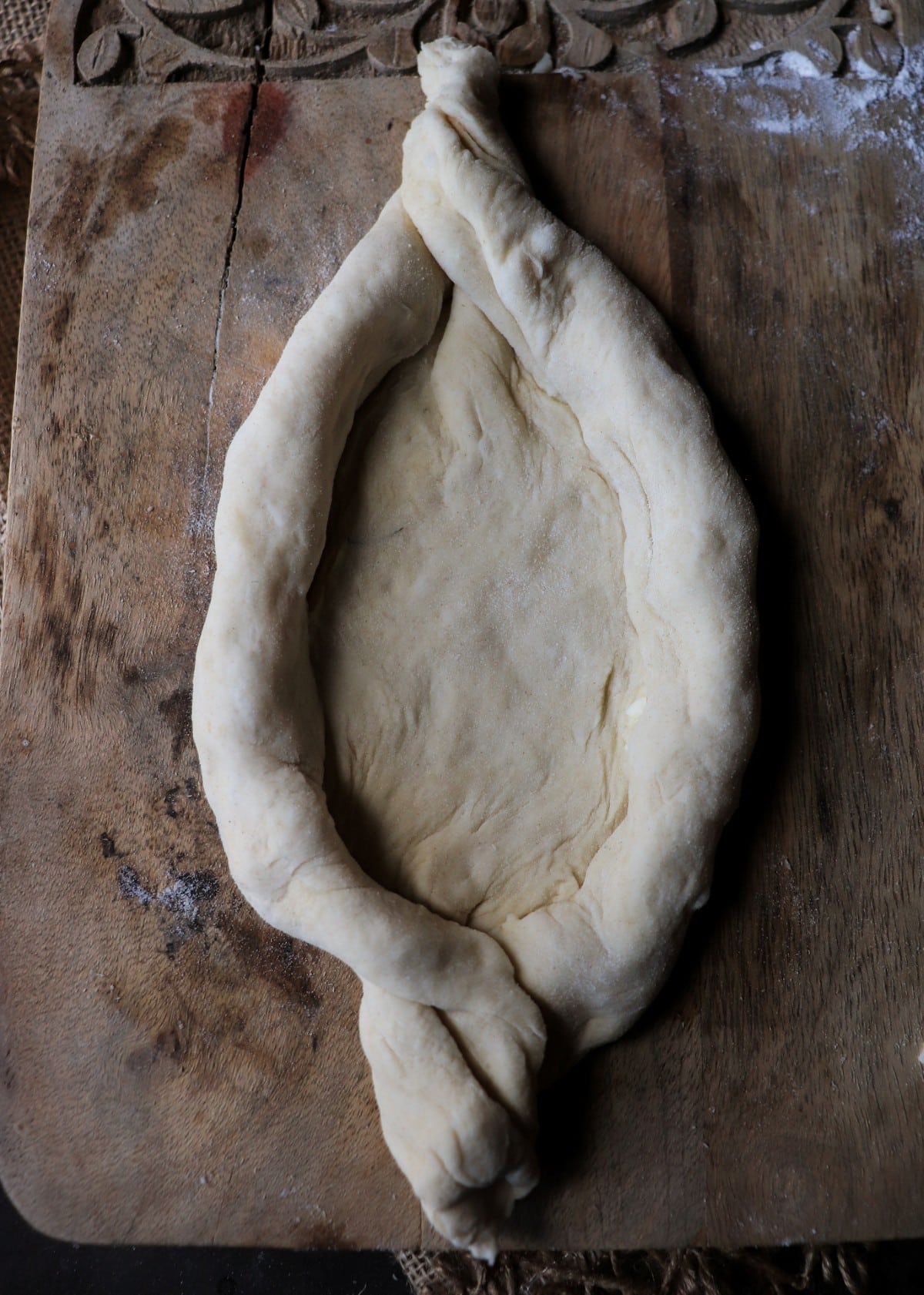 Forming traditional boat-shaped khachapuri with twisted ends