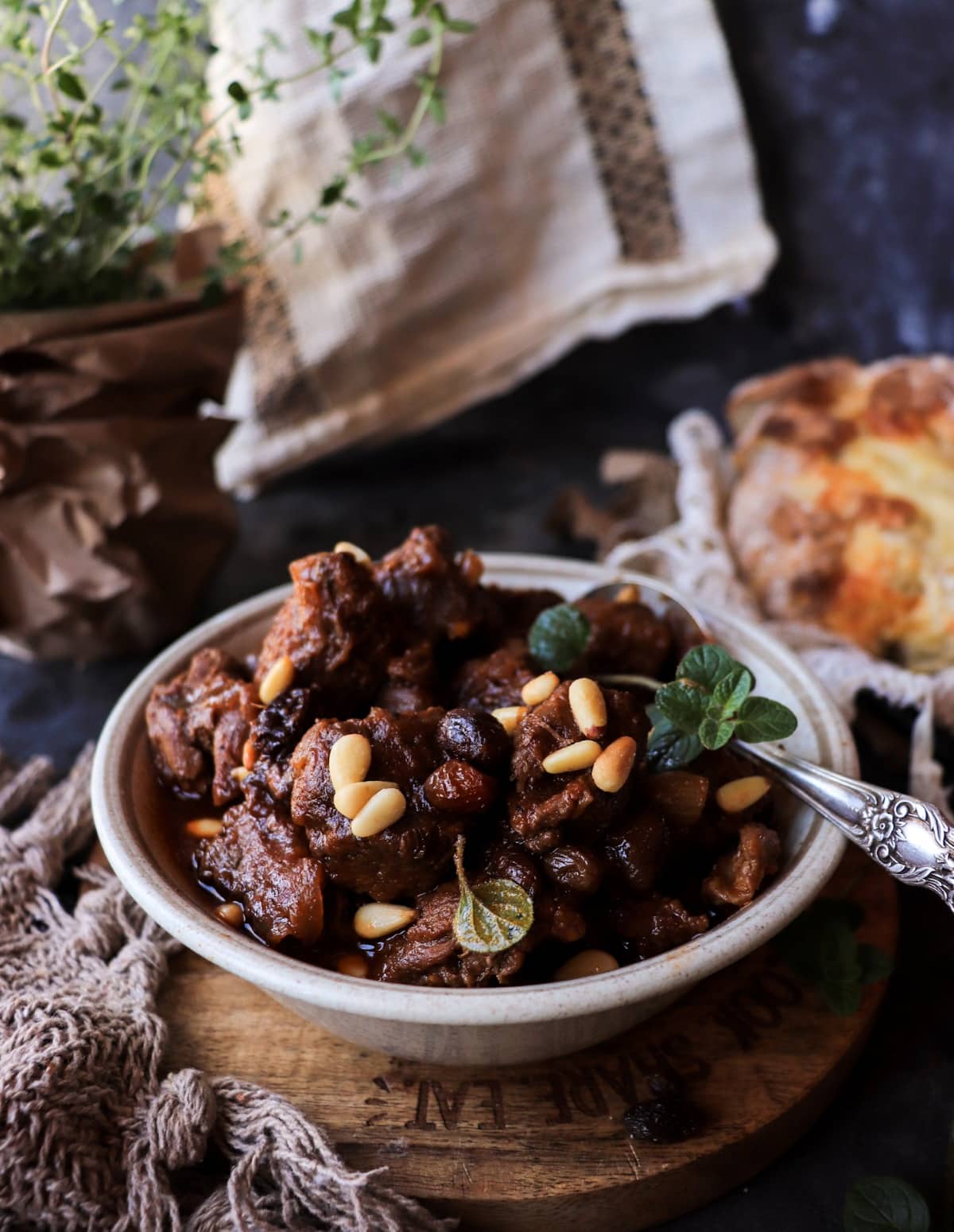 Close 45-degree view of Sicilian-inspired beef stew topped with pine nuts and served with crusty bread.