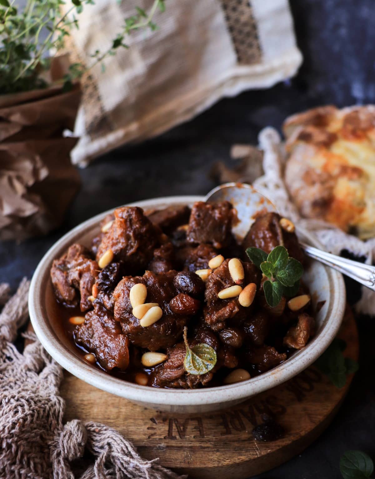 Close 45-degree view of Sicilian-inspired beef stew topped with pine nuts and served with crusty bread.
