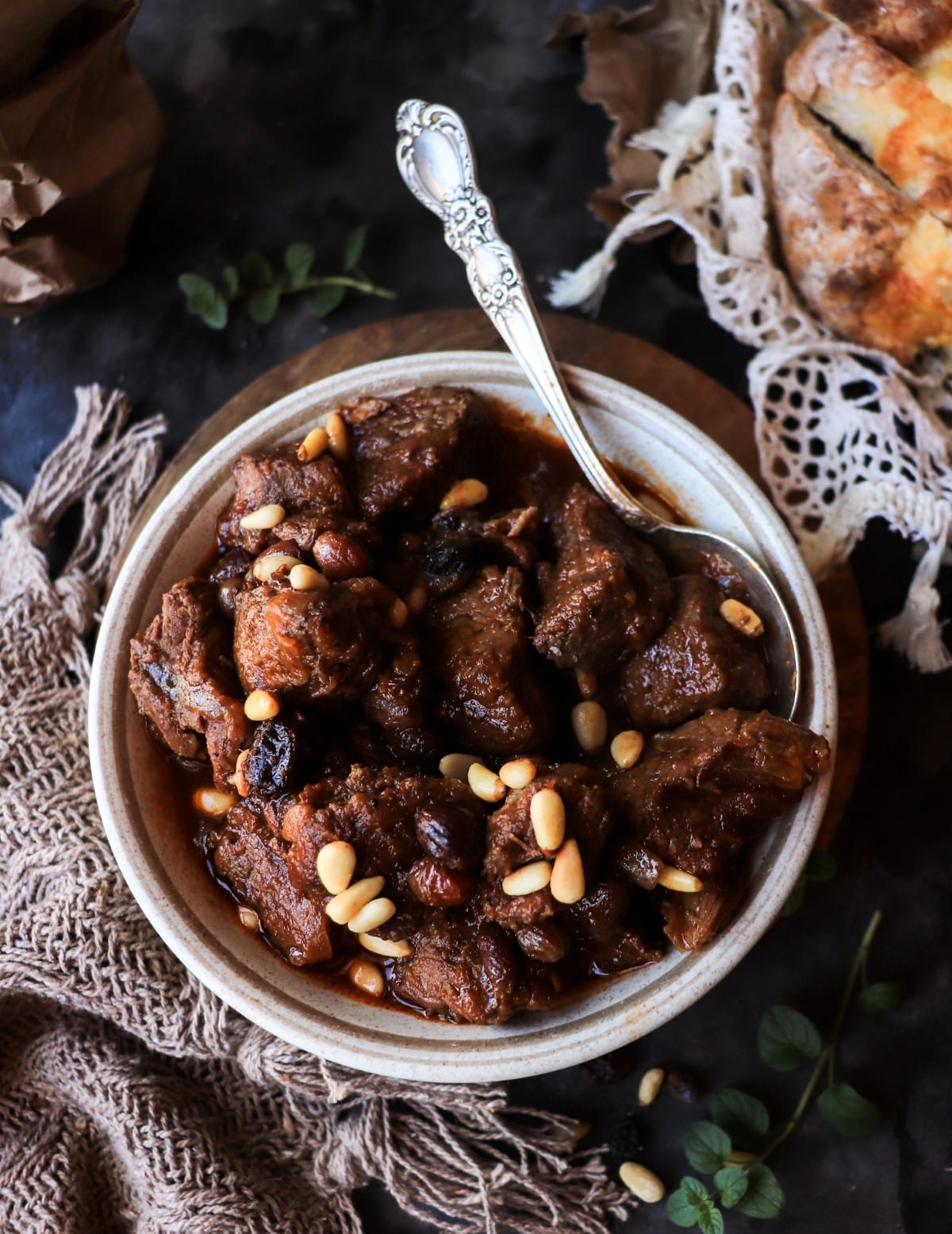 Overhead view of Sicilian-inspired beef stew with raisins and pine nuts in a rustic bowl on a wooden board.