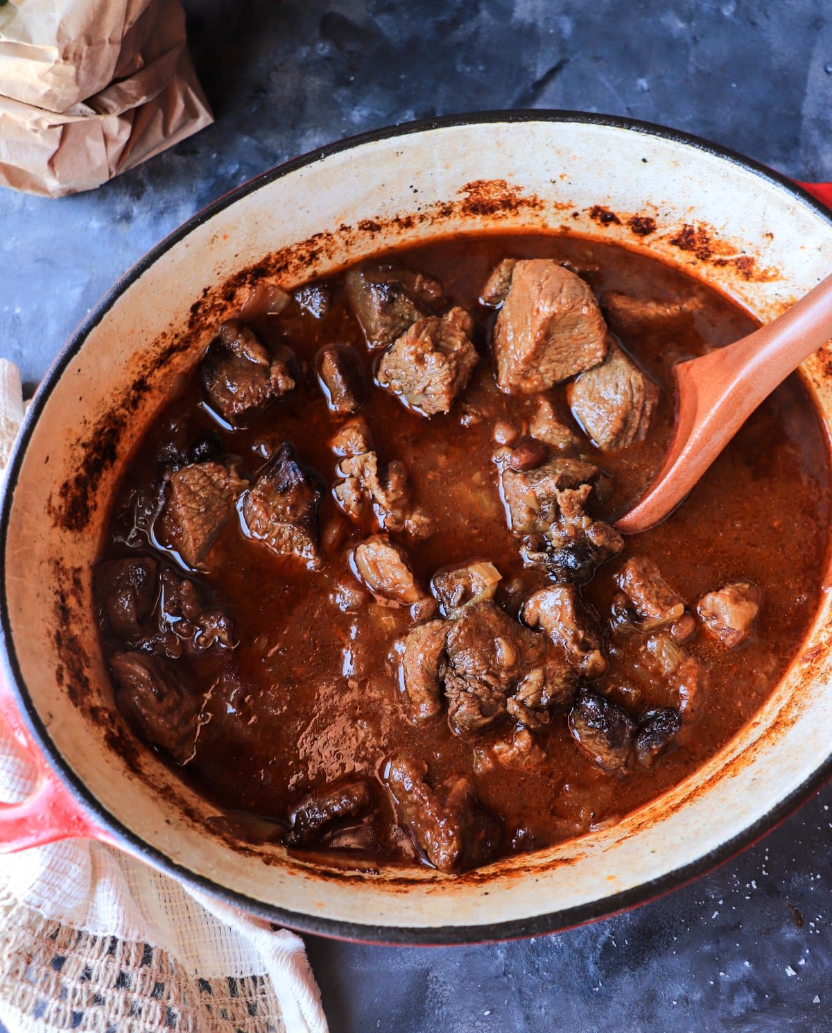Sicilian-inspired beef stew braising in a Dutch oven with tender beef, onions, and raisins in glossy sauce.